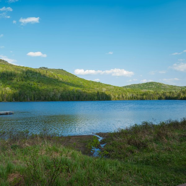 A swimming raft on a lake below green forested hills at Sainte-Lucie-des-Laurentides, in Quebec's Laurentians